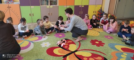 dzieci siedzą na dywanie i zawijają faworki z papieru