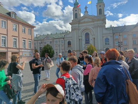 Grupa z przewodnikiem na placu przed pomnikiem powstańców warszawskich