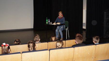Prowadząca czyta na scenie bajkę, uczniowie siedza na widowni