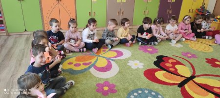 dzieci siedzą na dywanie i zawijają faworki z papieru