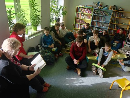Uczniowie siedzą na dywanie, bibliotekarki czytają tekst