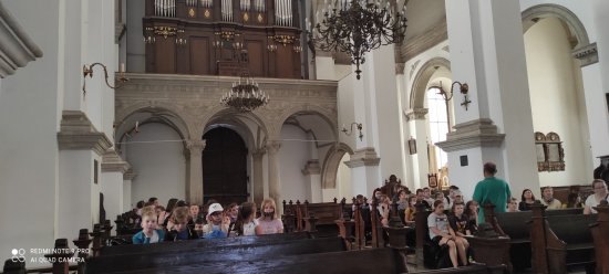 Wewnątrz katedry zamojskiej przewodnik opowiada historię , w ławkach siedzą uczestnicy 
