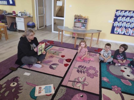 Bibliotekarka siedzi na dywanie i czyta dzieciom ksiązkę