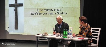 Na scenie za stołem siedzi autor i prowadząca, w tle prezentacja multimedialna