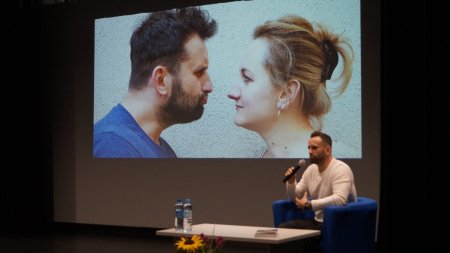 Na scenie siedzi autor, w tle wyświetlone zdjecie z żoną autora