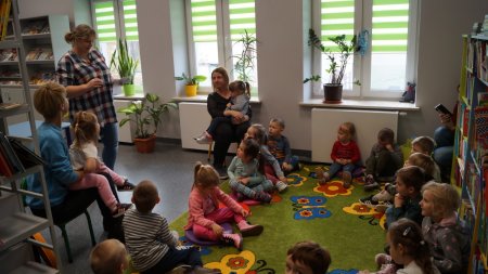 Bibliotekarka pokazuje siedzącym na dywanie dzieciom obrazki