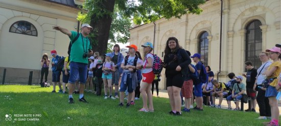 Na zdjęciu znajduje się przewodnik oraz grupa dzieci i młodzieży na tle katedry w Zamościu