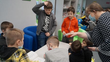 Dzieci siedzą w fotelach przy stoliku i rozmawiają